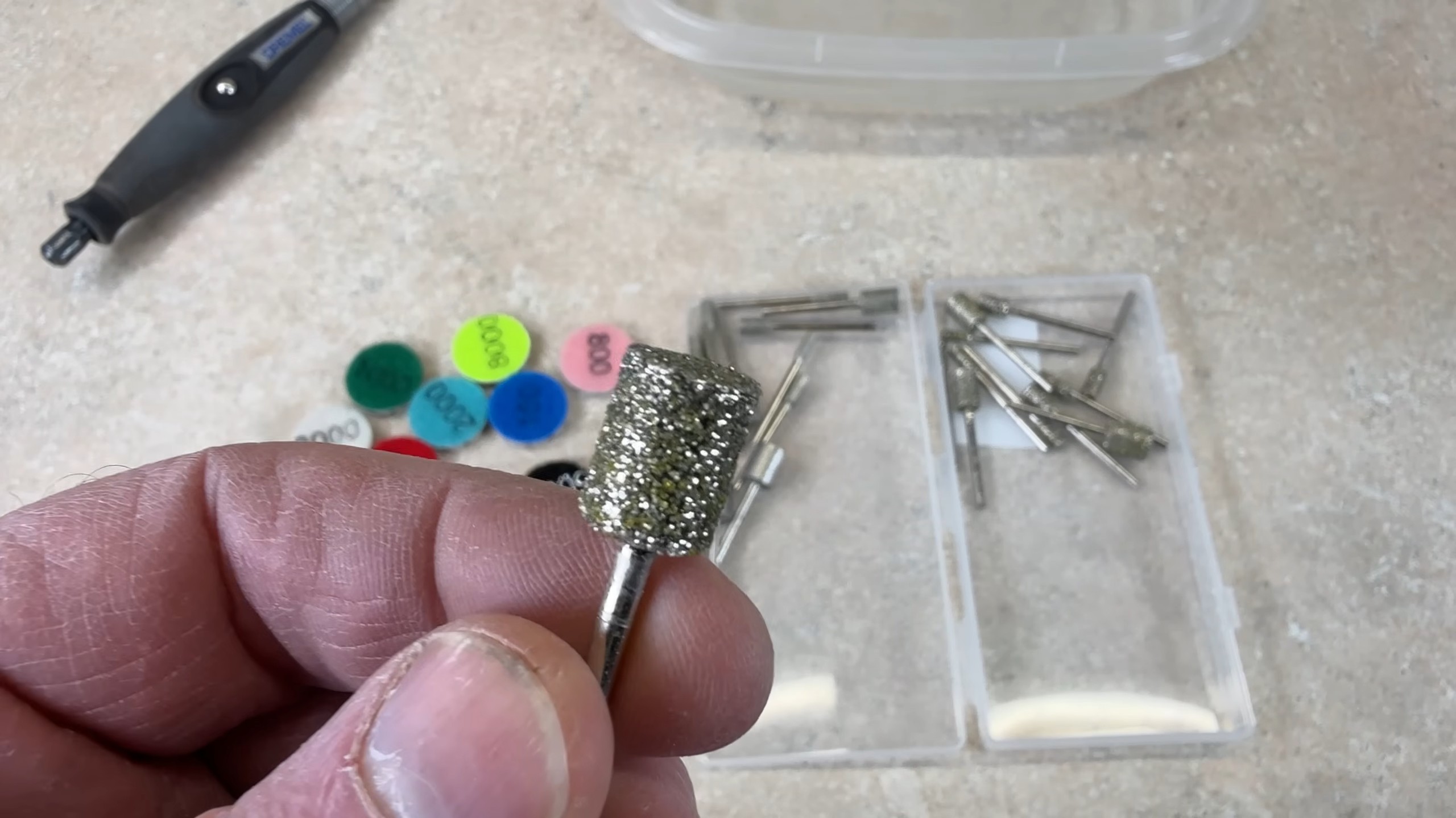 Diamond burr bit being selected from a tray of rotary-tool accessories and colored grit discs for rock polishing