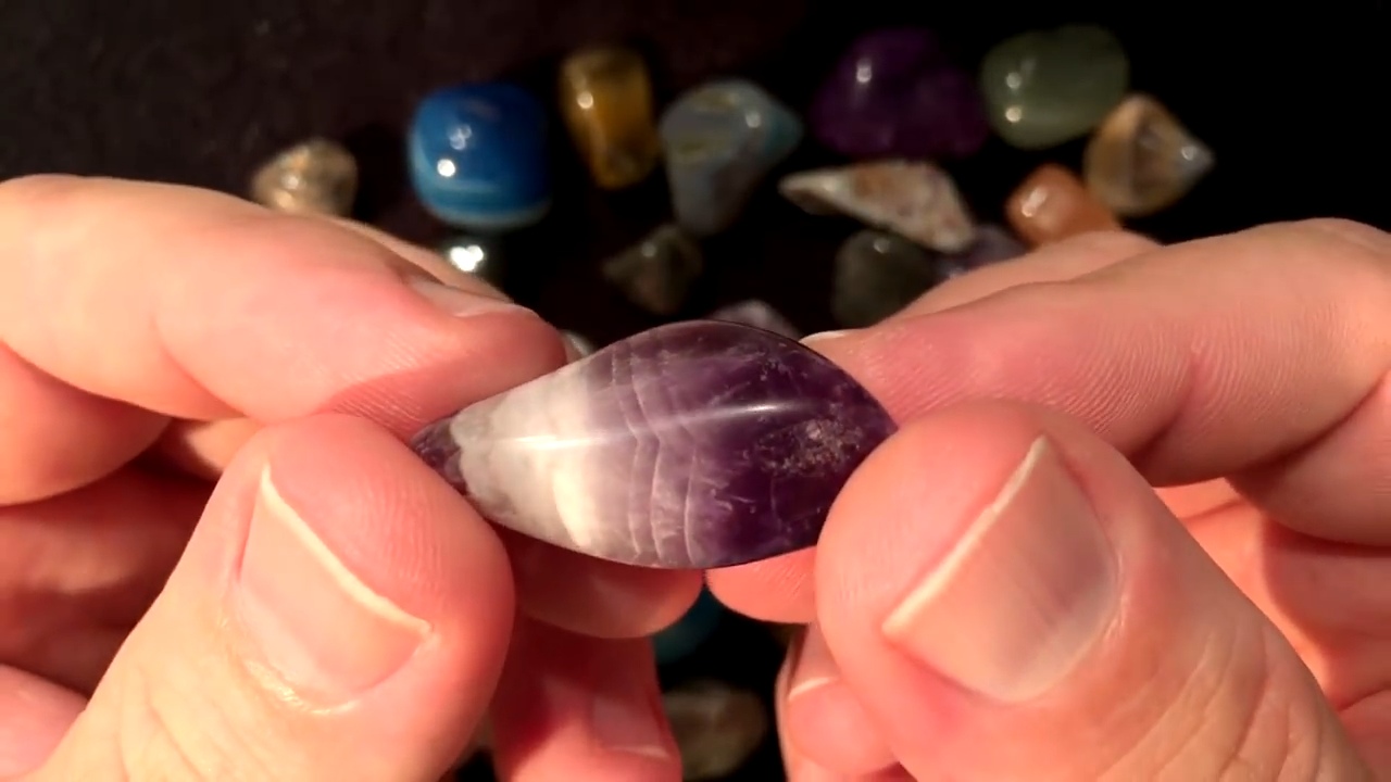 Chevron-banded tumbled amethyst held in fingers