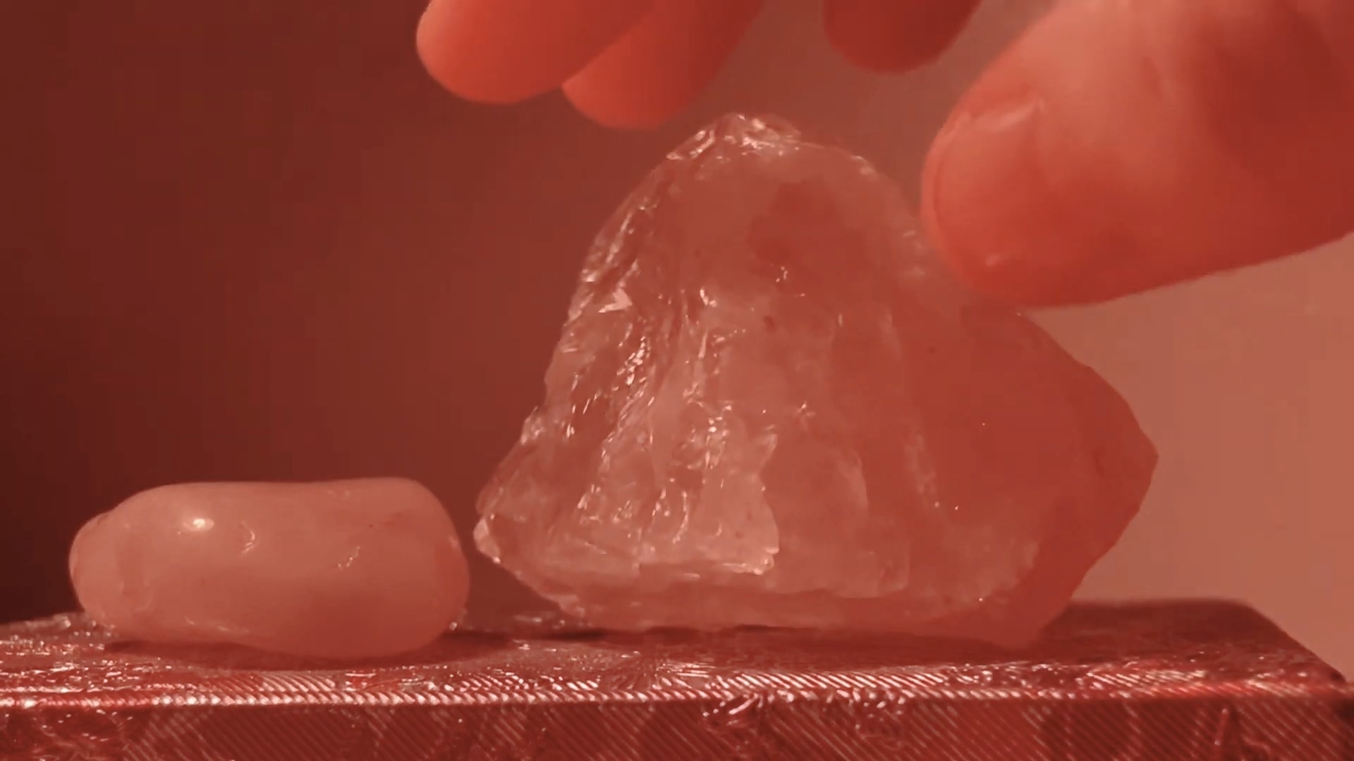 Tumbled rose quartz next to a larger raw specimen