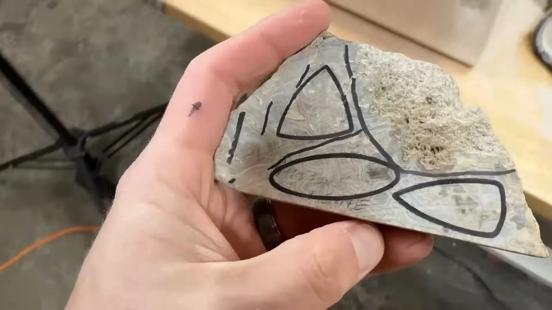 Crazy lace agate slab held in hand with four sharpie-drawn oval templates for cabochon cutting