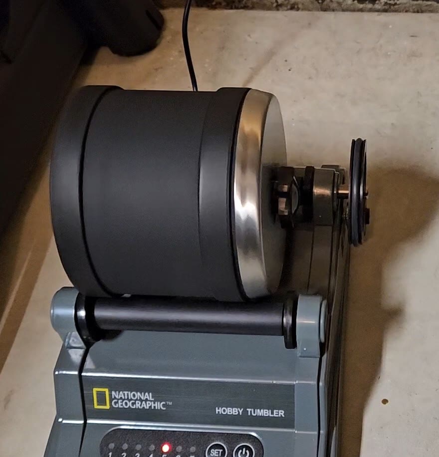 National Geographic Hobby Rock Tumbler running on its stand, showing the rubber barrel with stainless-steel lid, National Geographic branding, LED indicator panel, and drive pulley
