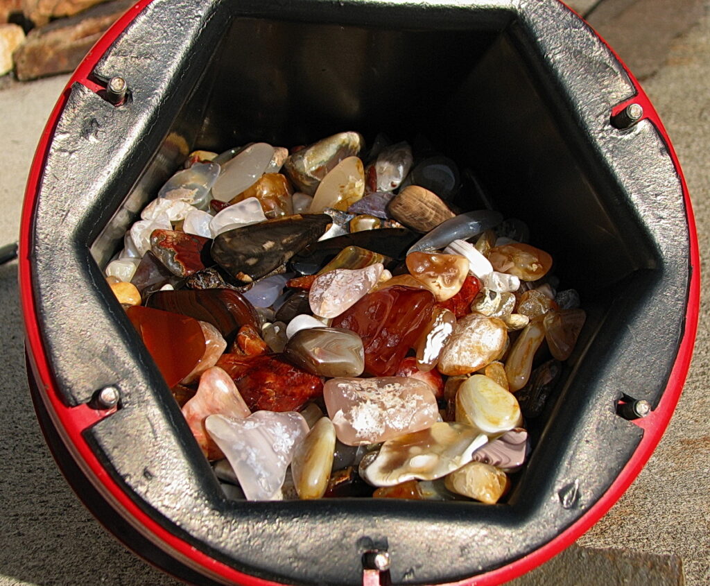 Tumbled agates and jasper glistening in an open rock tumbler barrel