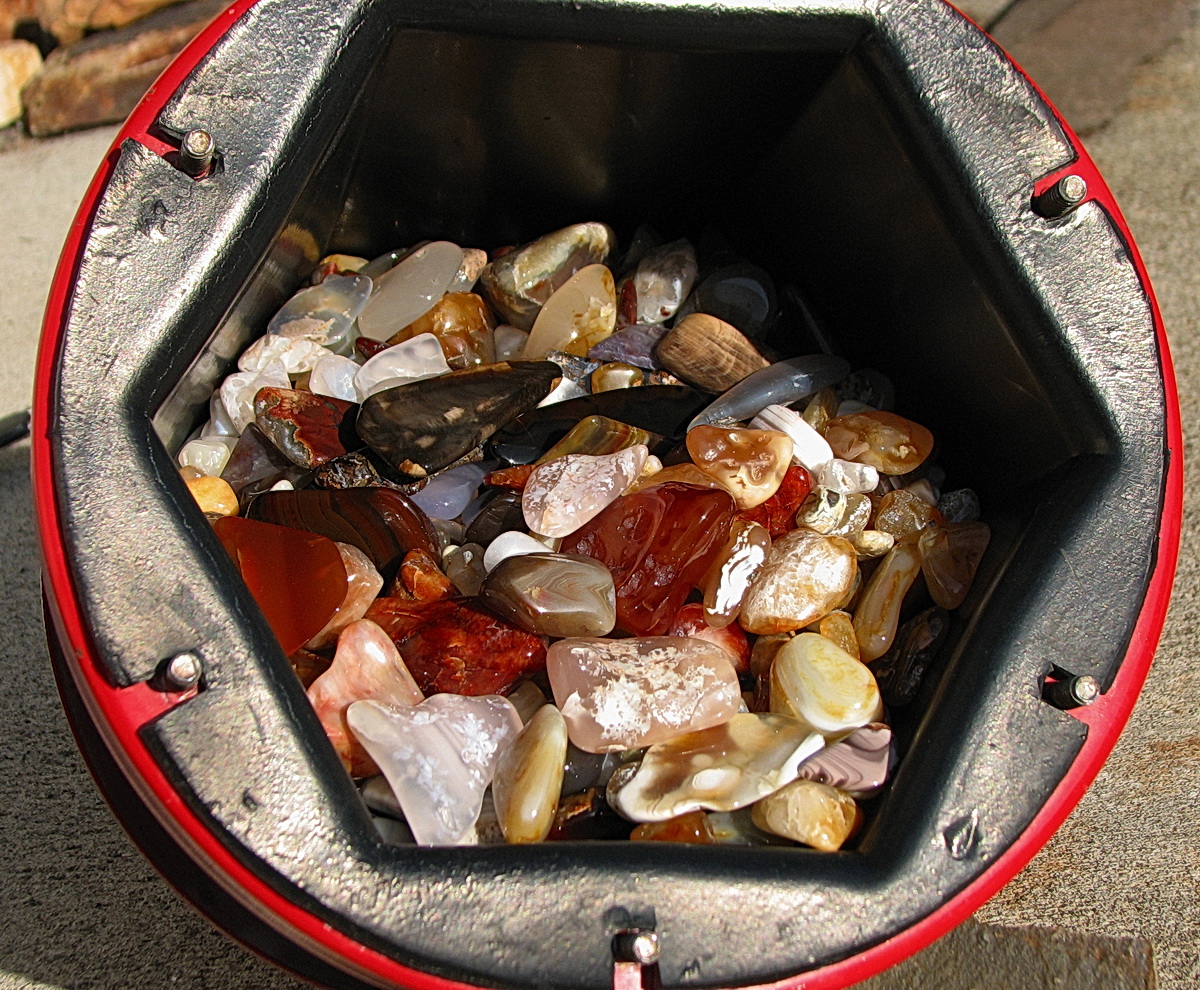 Tumbled agates and jasper glistening in an open rock tumbler barrel